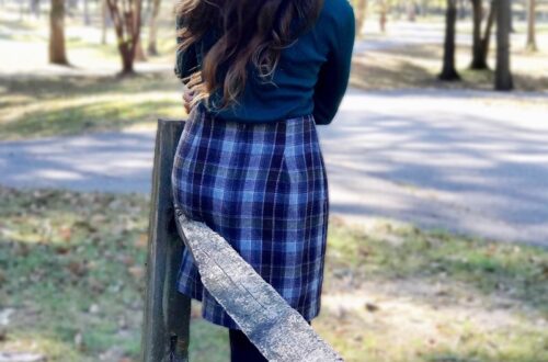 Woman standing in fall leaves wearing plaid wool skirt