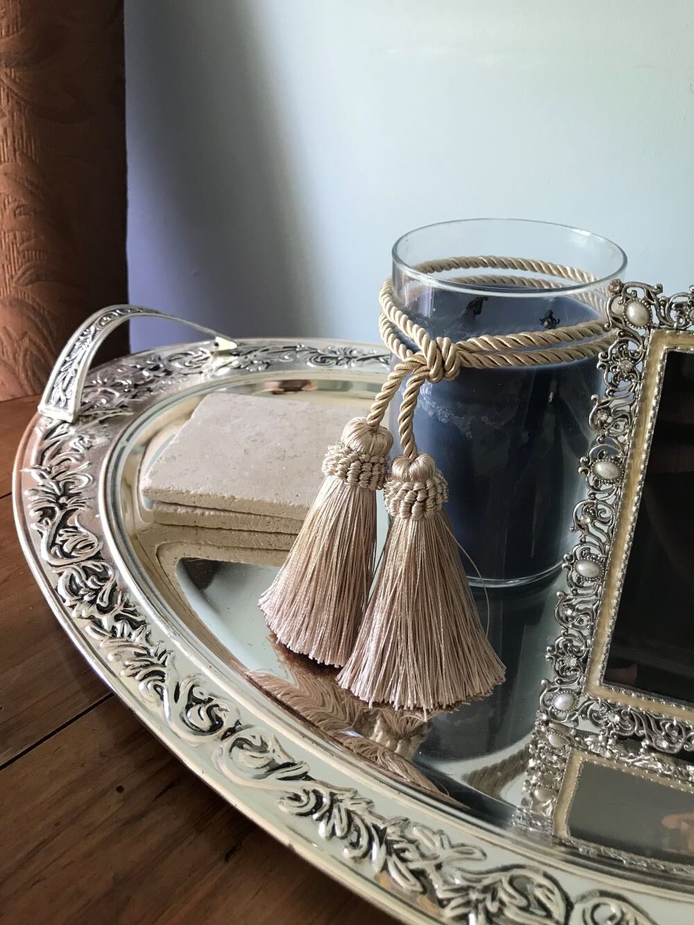 tray on a small table layered with a candle and tassel tied around it and a set of coasters and a picture frame